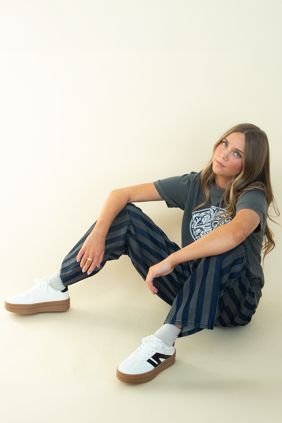 Seated model wearing dark-wash and gray striped wide-leg jeans with a relaxed silhouette and full-length leg.