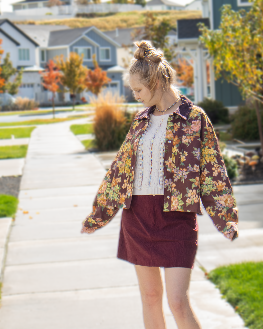 Model wearing a maroon floral collared jacket with large vintage-inspired flowers, front pockets, and snap-button closure.