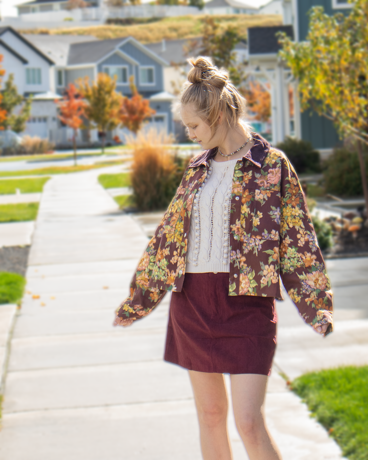 Model wearing a maroon floral collared jacket with large vintage-inspired flowers, front pockets, and snap-button closure.