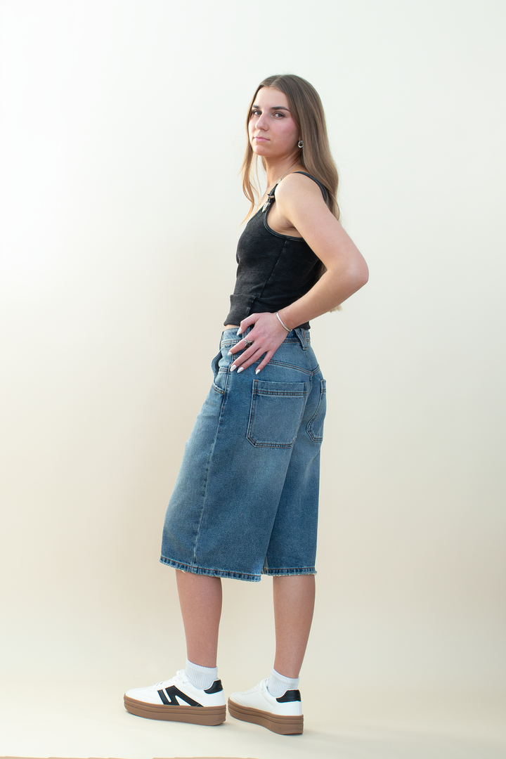 Side and back view of medium-wash denim Bermuda shorts with a relaxed longline fit and oversized back pockets.