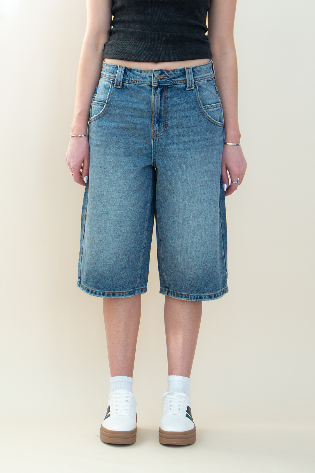 Close-up front view of medium-wash denim Bermuda shorts with a high-rise waist, five-pocket styling, and relaxed wide-leg fit.