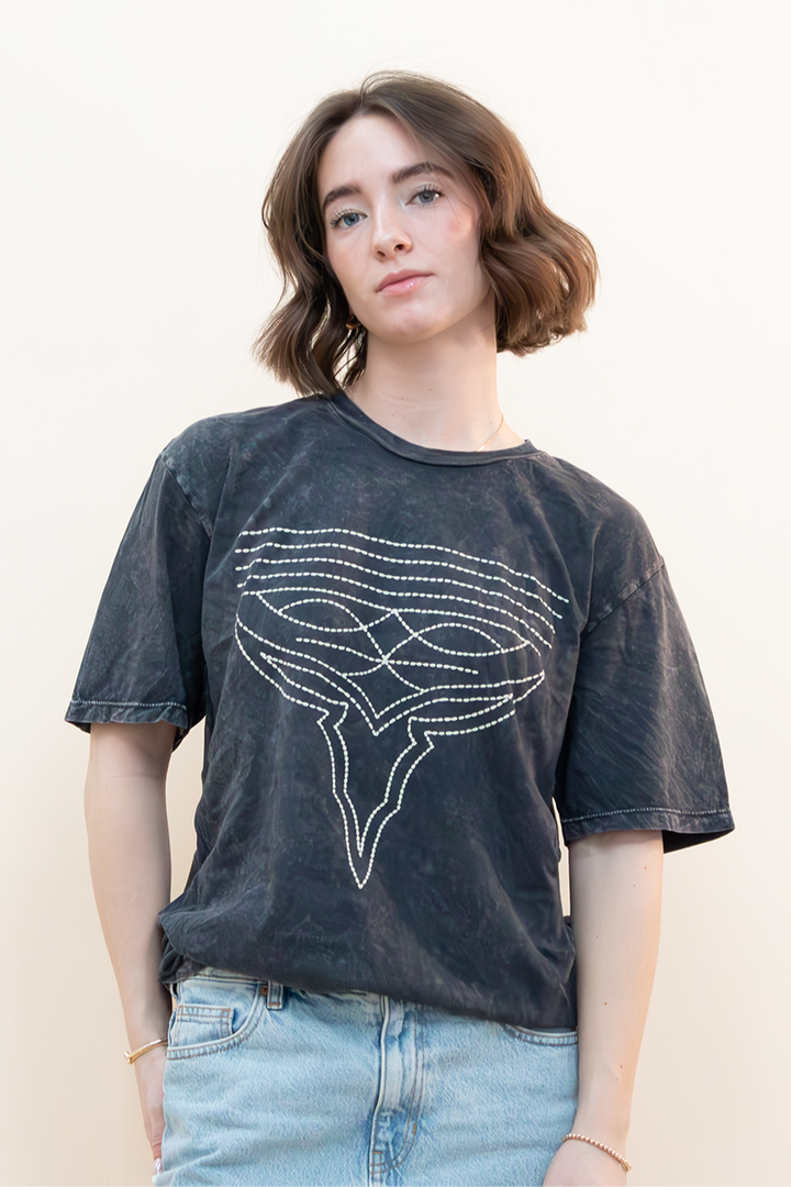 Woman wearing an oversized washed black graphic t-shirt with minimalist line art design, tucked into a light-wash denim skirt. Casual and effortless outfit styled for everyday wear by Groove Closet.