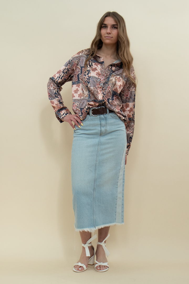Woman wearing a long-sleeve satin patchwork blouse with a button-up front, styled with a light denim midi skirt and white wrap heels—boho-inspired printed shirt perfect for women’s fall fashion or casual chic looks.