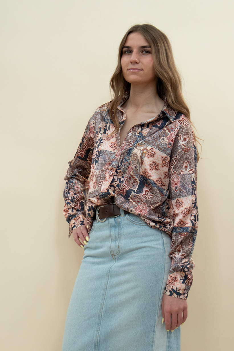 Woman wearing a boho-style satin button-up blouse with a mixed floral and paisley patchwork print in warm tones, paired with a high-waisted light wash denim skirt—versatile long sleeve top for casual and statement outfits.