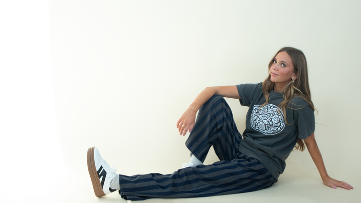 Model wearing dark-wash and gray vertically striped wide-leg jeans with a relaxed fit, styled with a charcoal graphic tee and white sneakers.