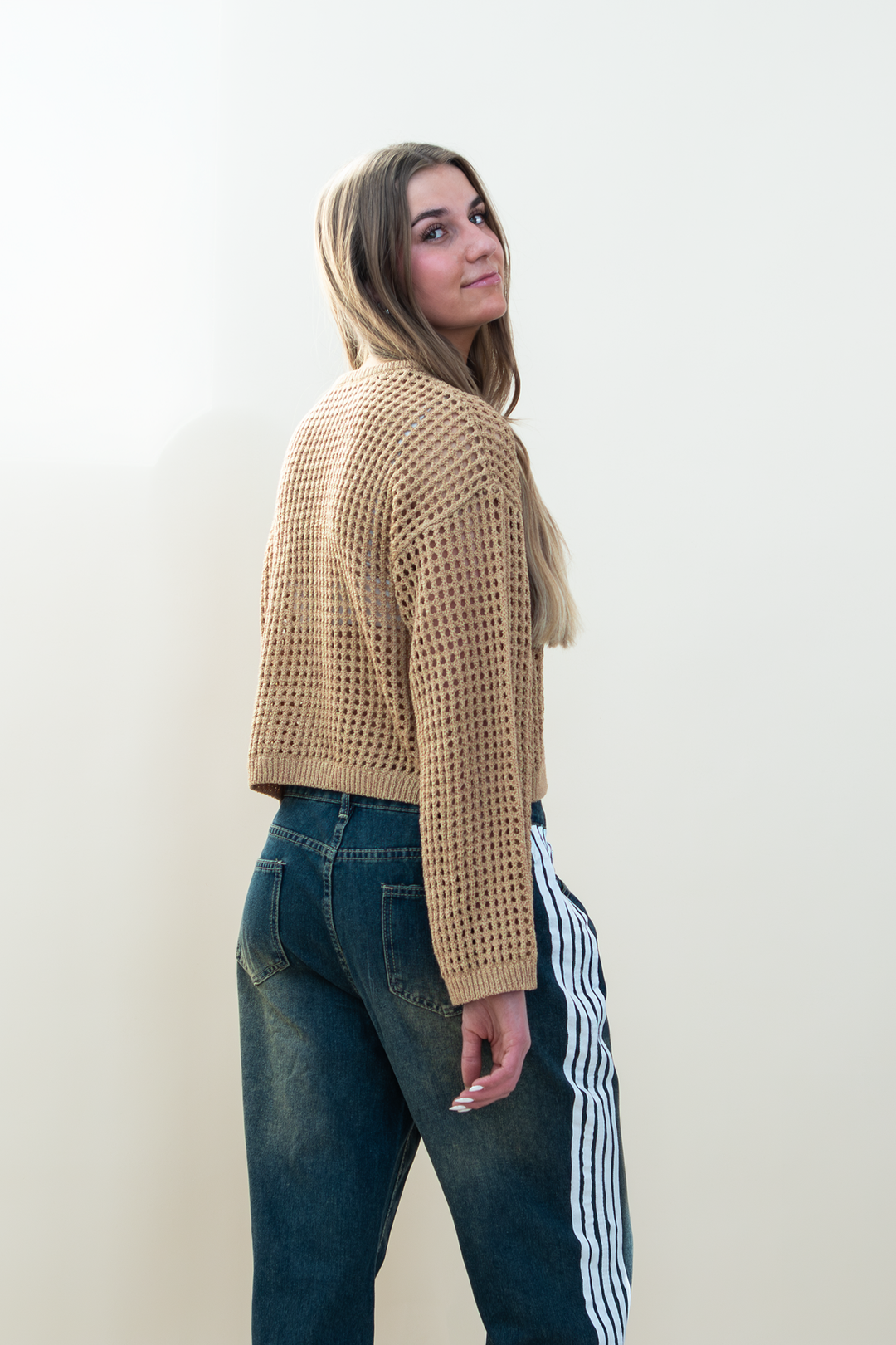 Three-quarter back view of tan open-knit cropped sweater showing the airy mesh knit and relaxed long-sleeve fit.