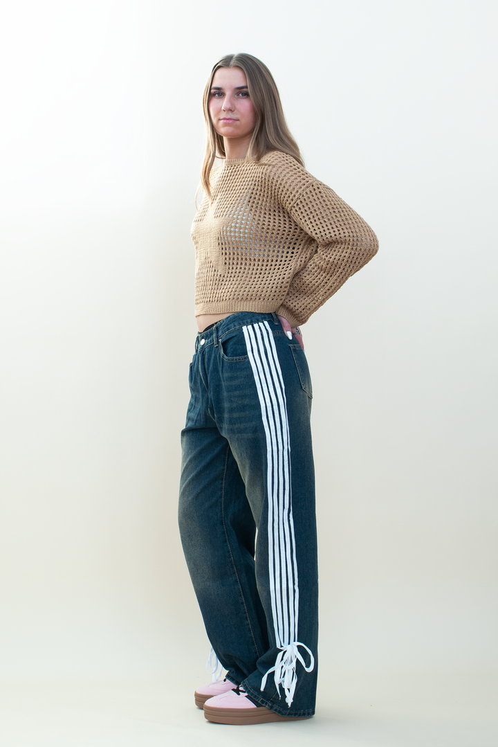 Side view of model wearing a tan open-knit cropped star sweater with dark wash wide-leg jeans featuring white side stripes and lace-up ankle ties.